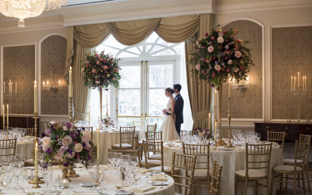 Bride and Groom standing in banqueting hall at The InterContinental Dublin. The room is set up for the wedding celebration with beautiful floral centerpieces on each table.