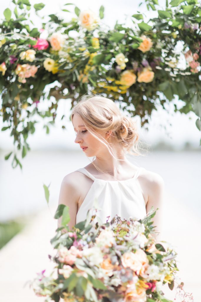 bride holding a bouquet of mixed flowers below a display of more flowers