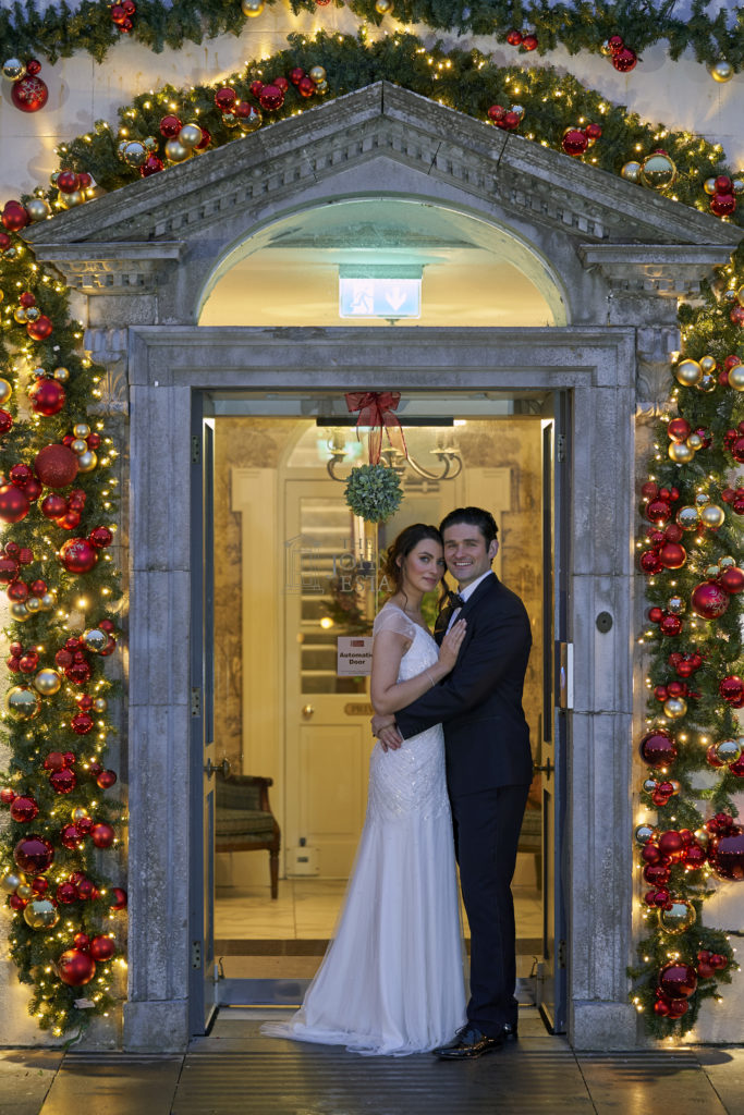 Bride and Groom standing at main door of Johnstown Estate. The door is surrounded by Christmas decorations and lights.