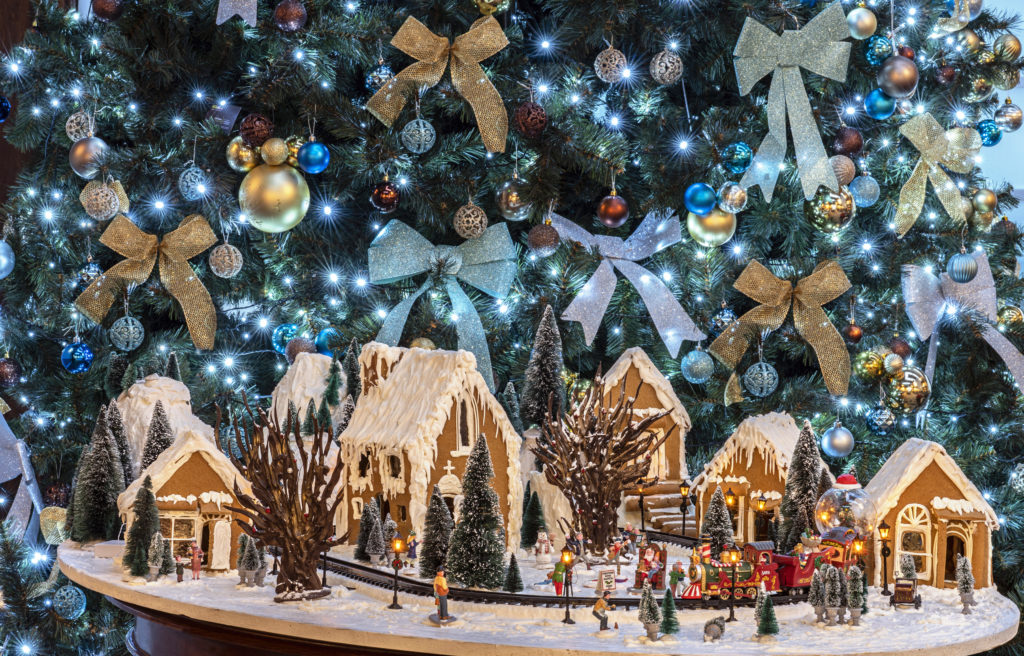 Gingerbread Village with Christmas tree visible in the background.