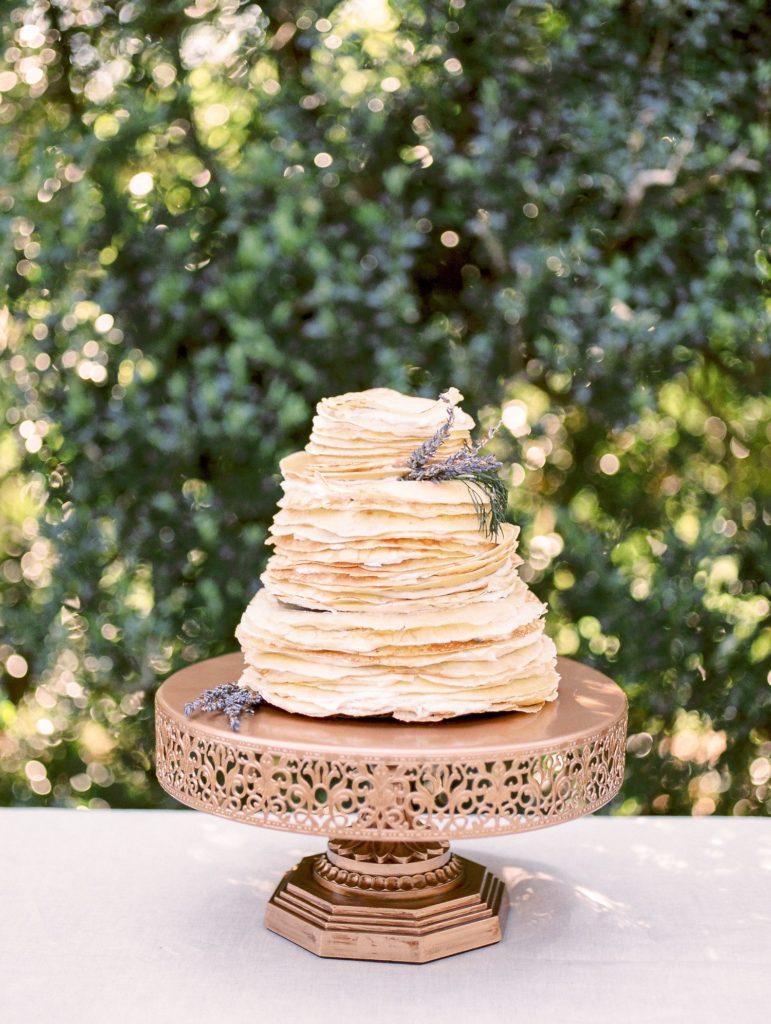 A three tier stack of pancakes held together with icing and presented on a bronze cake stand with fresh lavender decorations