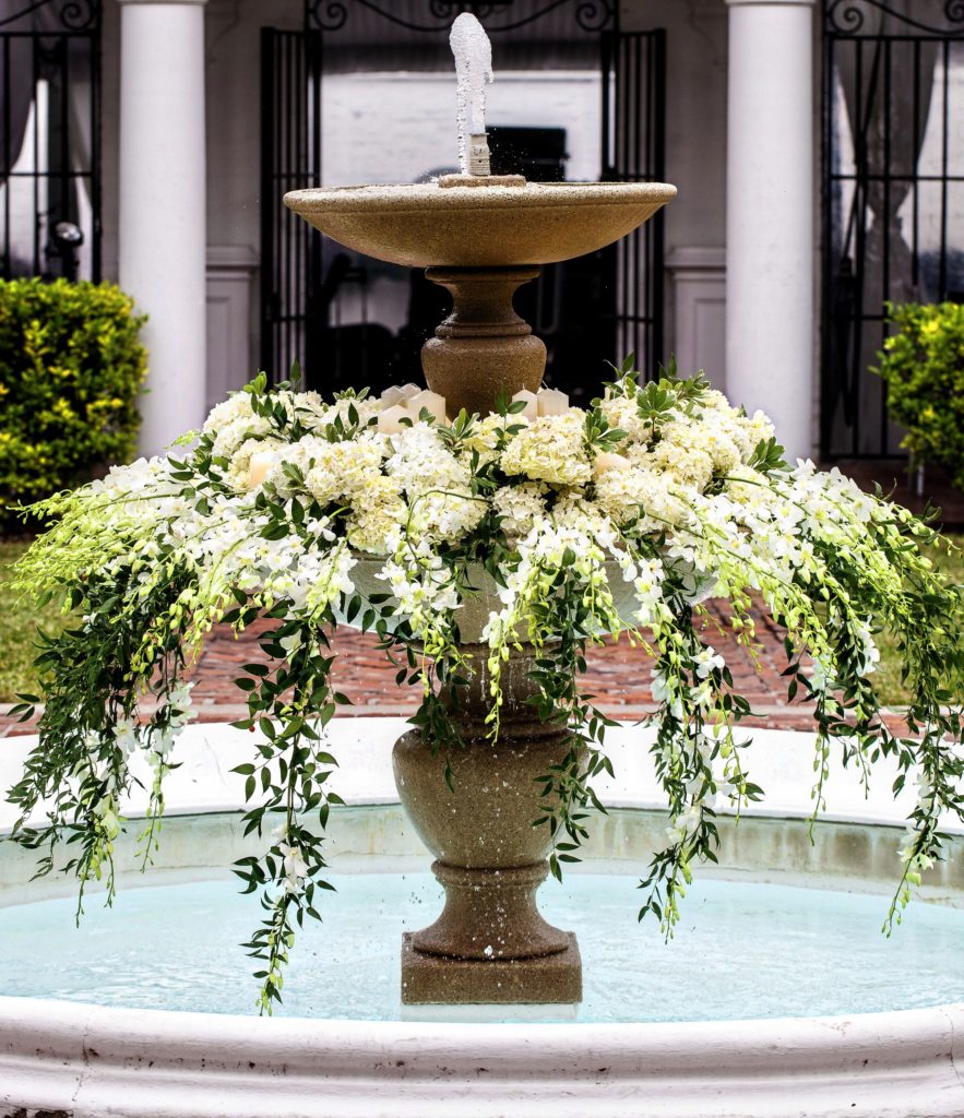 Gold, two tier fountain filled with white flowers and hanging greenery and water