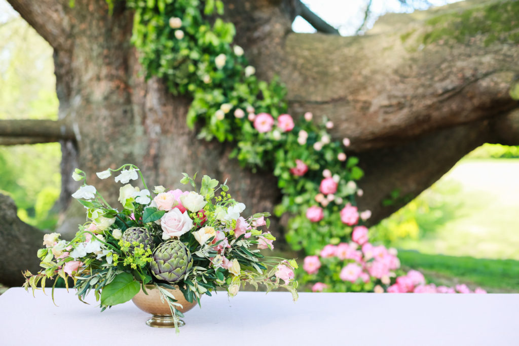 Medium sized table display of pink and white flowers, succulents and greenery displayed in a shallow gold bowl on a white table cloth