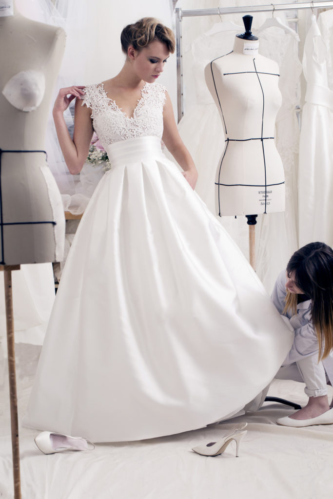 Bride in floor length, white satin, wedding dress with lace bodice and short sleeves having the skirt of her dress altered