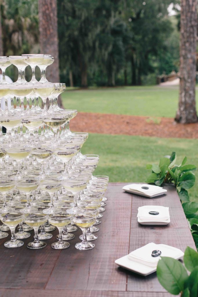 A pyramid of champagne glasses on a dark wood table in a well maintained garden 