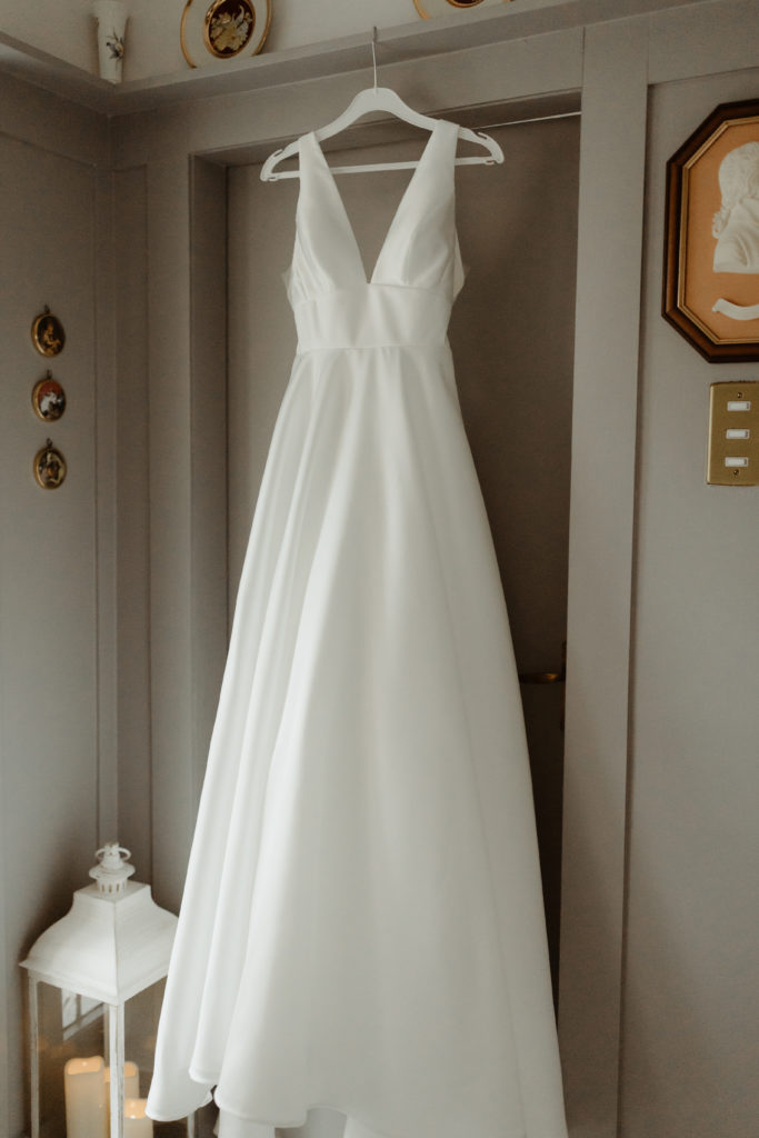 White Sassi Holford satin wedding dress hung up on a doorframe with a wooden hanger