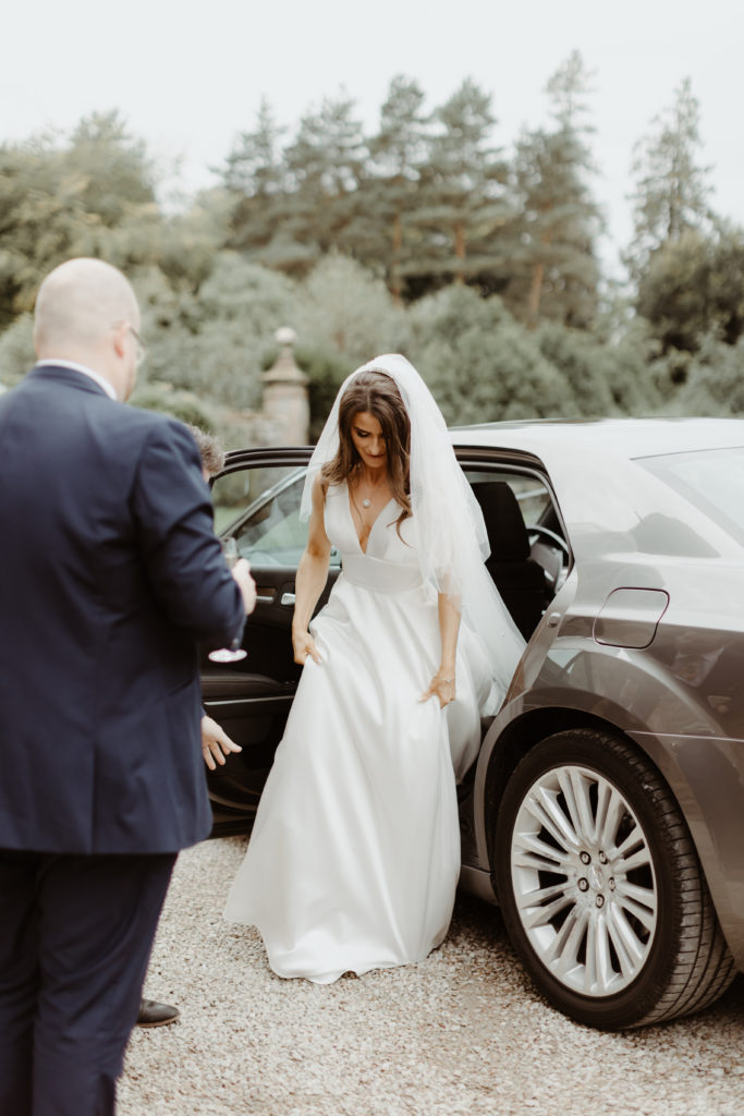 Irish bride getting out of a grey car in a white satin Sassi Holford wedding dress