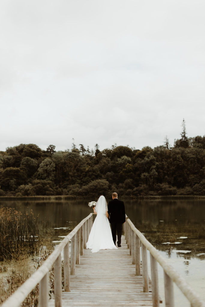 Irish bride and groom walking on a wooden pontoon over the lake on the grounds of Castle Leslie in Ireland