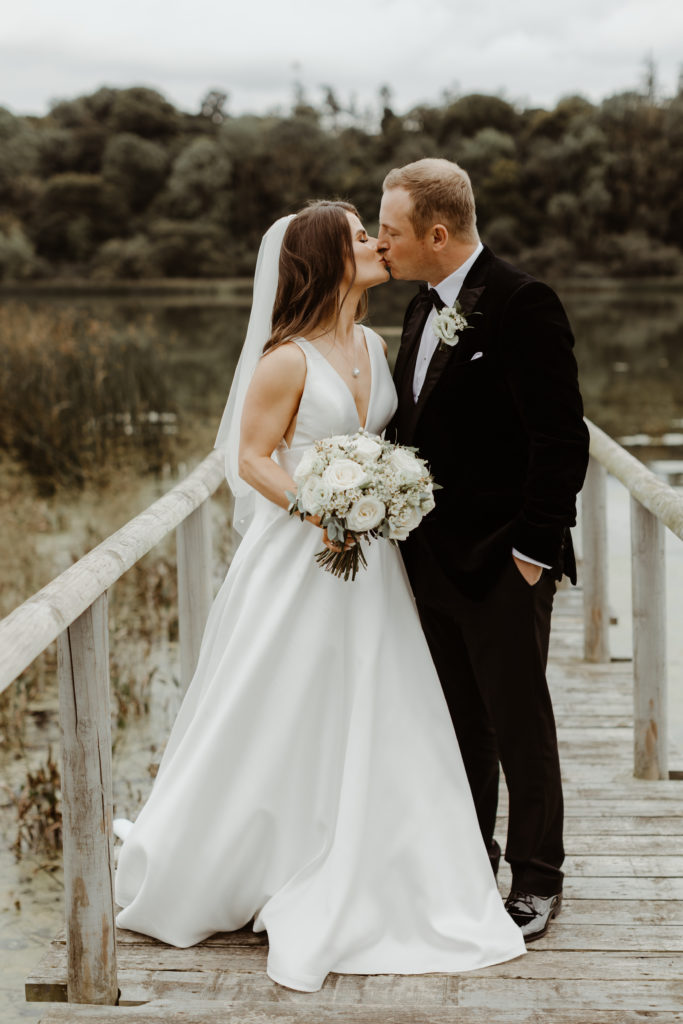 Irish bride and groom kissing in front of the lake on the grounds of Castle Leslie in Ireland