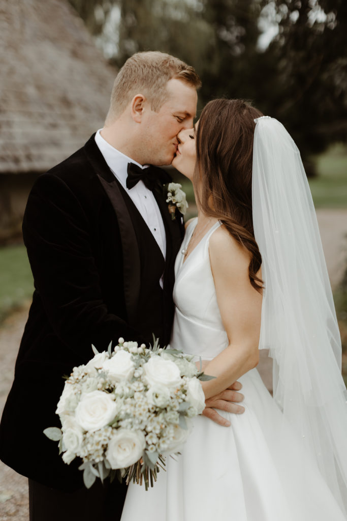 Irish bride and groom kissing in front of a grey stone building on the grounds of Castle Leslie in Ireland