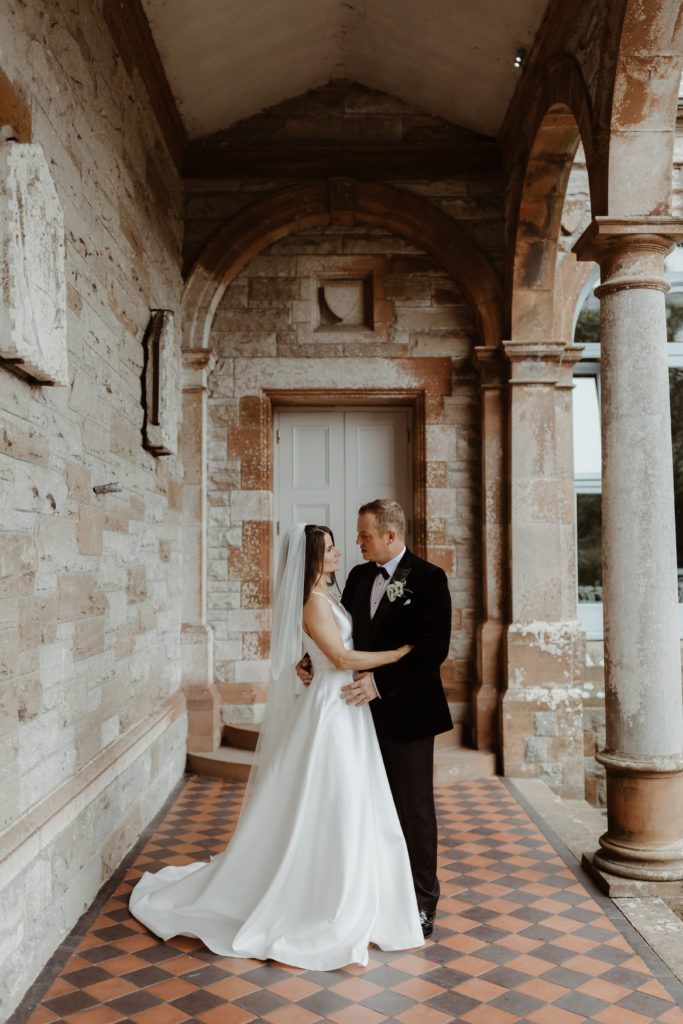 Irish bride and groom embracing in in a grey and red stone building on the grounds of Castle Leslie in Ireland