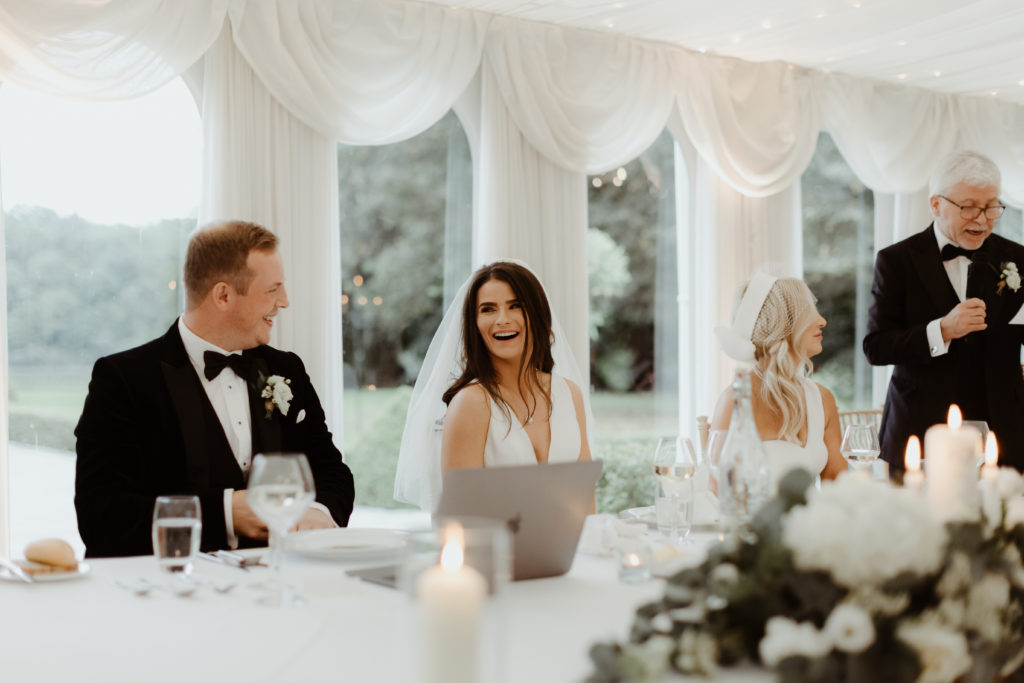 Bride and groom sitting at their wedding table laughing together during the father of the bride speech